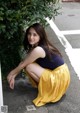 A woman sitting on the ground in front of a bush.