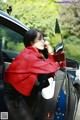 A woman in a red coat leaning out the door of a car.