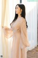 a woman standing in front of a window wearing a beige dress