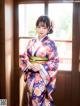 A woman in a kimono standing in front of a window.