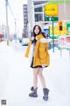 A woman in a yellow coat is standing in the snow.