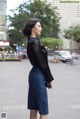 A woman in a black shirt and blue skirt is standing on the street.