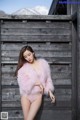 A woman in a pink fur coat leaning against a wooden fence.