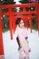 A woman in a pink kimono standing in front of a red gate.