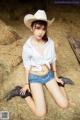 A woman in a cowboy hat sitting on a pile of hay.