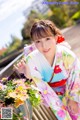 A woman in a kimono sitting on a bench with flowers.