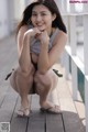 A woman sitting on a wooden deck with her hands on her chin.