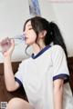 A woman in a white shirt is drinking water from a bottle.