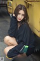 A woman sitting on the ground in front of a yellow truck.