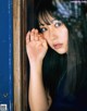 A woman with long black hair leaning against a blue door.