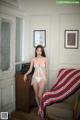 A woman in a white lingerie standing next to a chair.