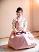 A woman in a pink and white hanbok sitting on the floor.