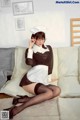 A woman in a maid outfit sitting on a couch.