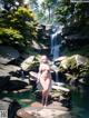 A naked woman standing in front of a waterfall.