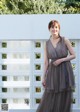 A woman in a gray dress standing in front of a white wall.