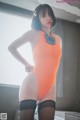 A woman in an orange bodysuit and black stockings posing for a picture.