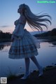 A woman in a white dress standing by a body of water.