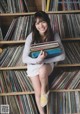 A woman sitting on top of a bookshelf holding a stack of records.