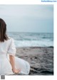 A woman in a white dress sitting on the beach.